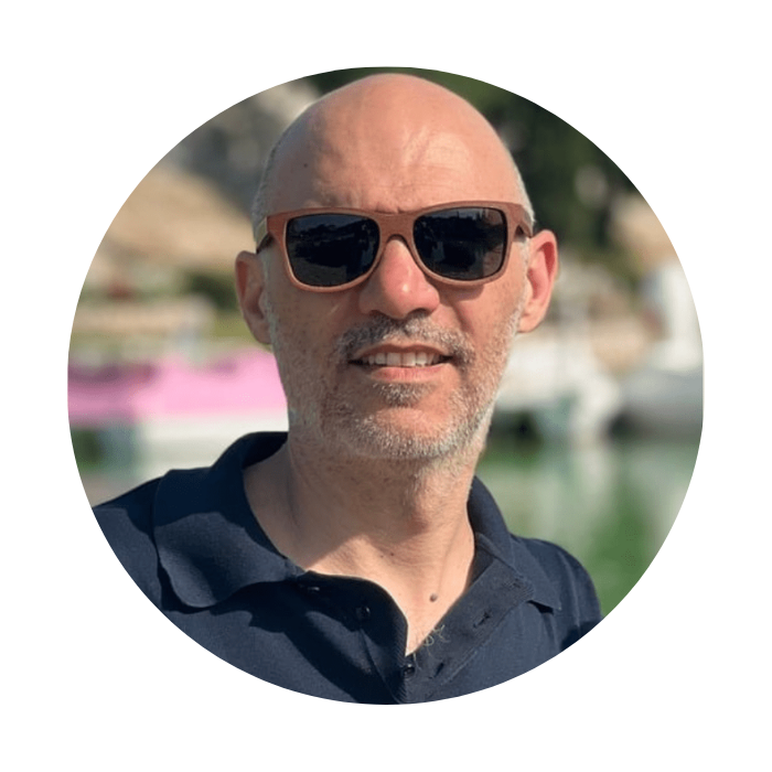 Man wearing sunglasses and a dark polo shirt with a blurred outdoor background