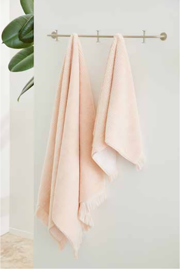 Plush 650-GSM Cotton Terry Towel in pink, an organic cotton towel with eyelash fringe, hanging on a towel hanger, showcasing its soft texture and elegant design.
