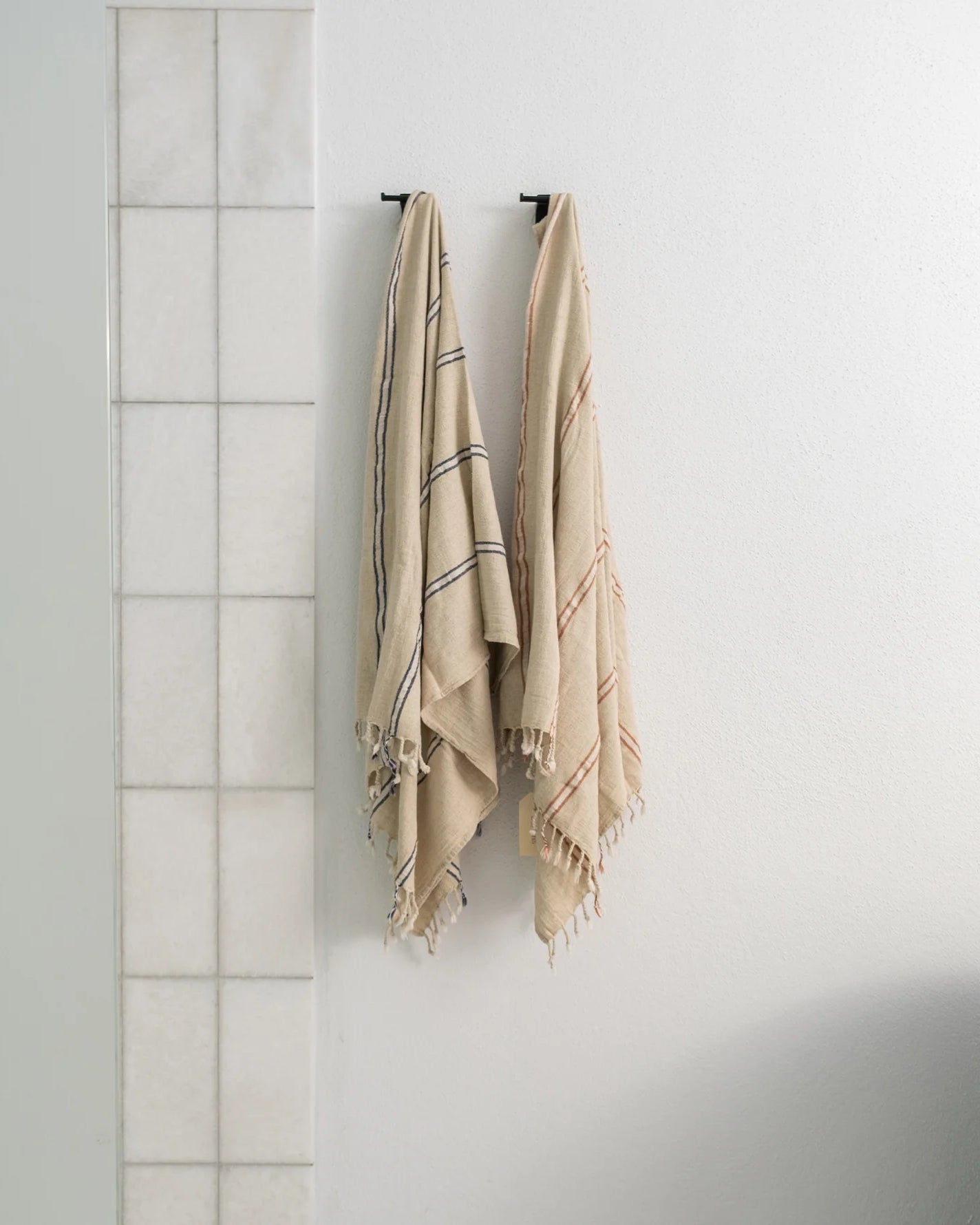 Two sustainable luxury Anakao 215 gram Aegean Cotton and Linen Turkish luxury bath towels hanging on a bathroom wall showcasing their soft texture and premium quality