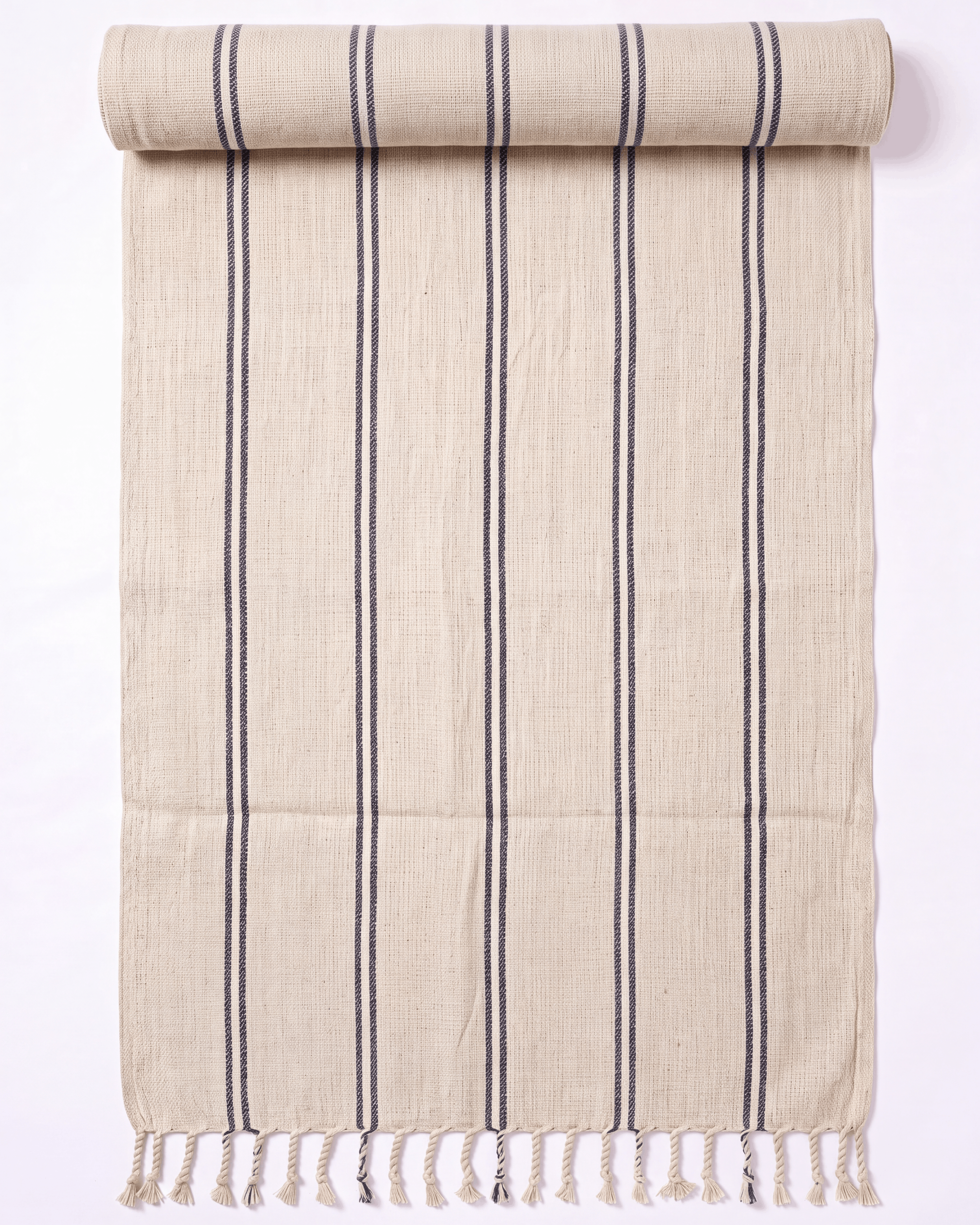 A beige woven towel with vertical dark gray stripes and fringed tassels along one edge, shown partially rolled on a plain white background.