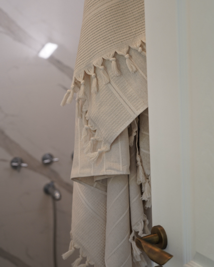 Beige textured towel with tassels hanging on a door handle in a bathroom.