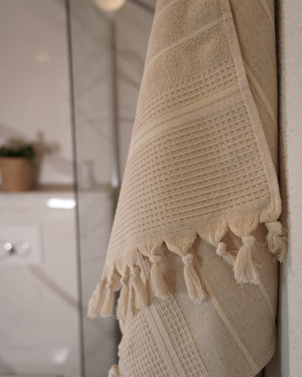 Beige towel with tassels hanging on a bathroom wall