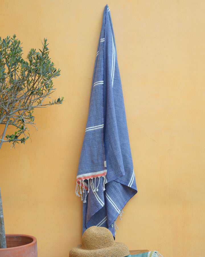 Blue towel hanging on a yellow wall next to a potted plant and straw hat.