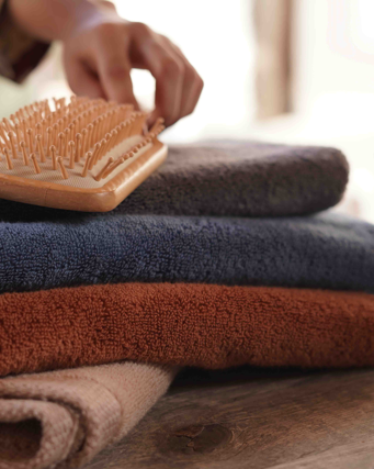 Side view of a large size Plush Lite 500-Gram Turkish Aegean Cotton luxury bath towel on a wooden table with a natural bristle brush on top, showcasing its soft texture and elegant design