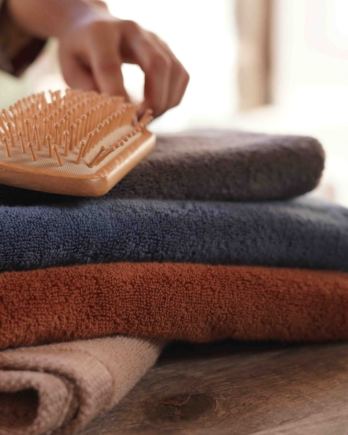 Minoa USA Canada sustainable luxury bath towels Plush Lite Aegean Cotton bath towel pack of four with a brush on top, highlighting soft texture, premium quality, and elegant design