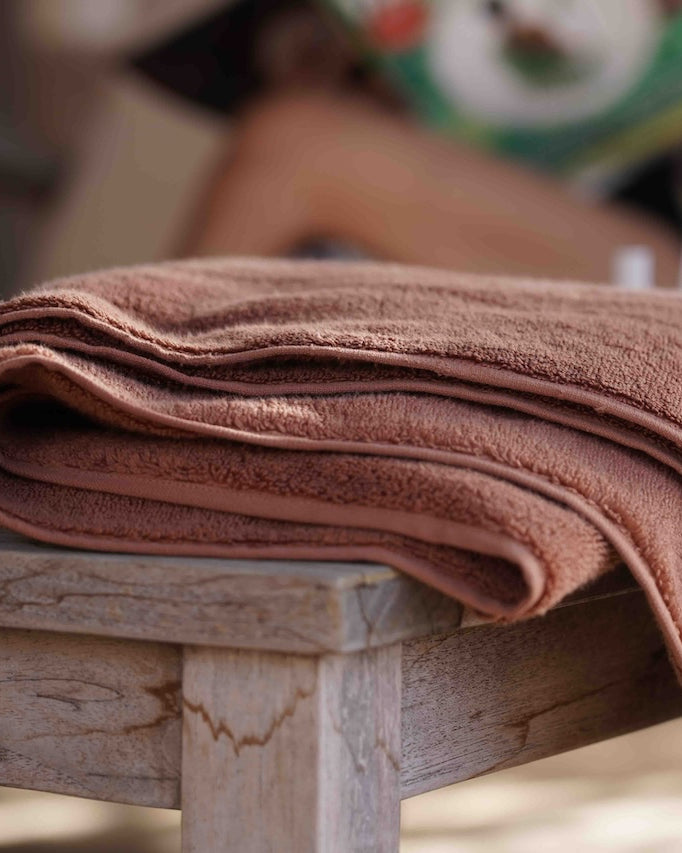 CinnamonCharm Plush Lite Aegean Cotton towel neatly folded on a wooden table, highlighting its warm tones and plush texture