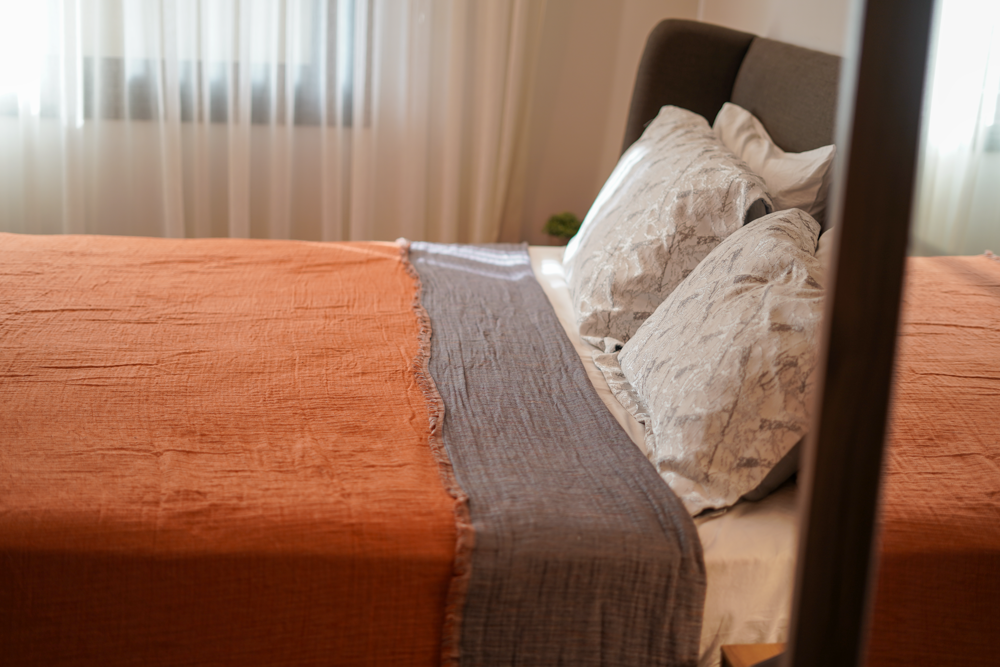 Reversible Muna organic gauze bed spread in Terra, draped on bed, soft texture, warm earthy hue, elegant design with organic cotton sheets.