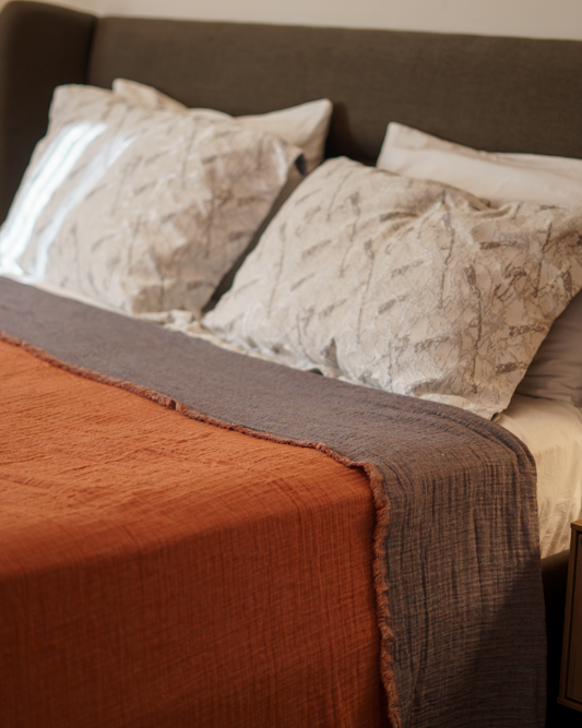 Reversible Muna organic gauze bed spread in Terra, draped on bed with soft texture, earthy hue, and elegance with organic cotton sheets.