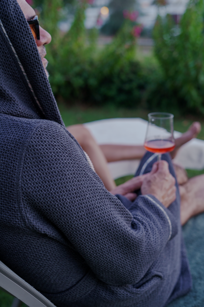 A male holding a glass of wine chilling with Minoa's luxuriously soft, organic Naia Panama Weave Mens Robe that provides extra comfort