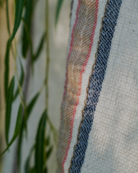 A close-up shot of the luxury organic Elba Turkish towel hanging on a cloth hanger outside, surrounded by green leaves for a natural vibe