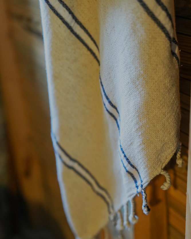 Blue and white eco friendly Anakao 215 gram Aegean Cotton and Linen Turkish towel hanging on wooden wall highlighting organic bath towel quality