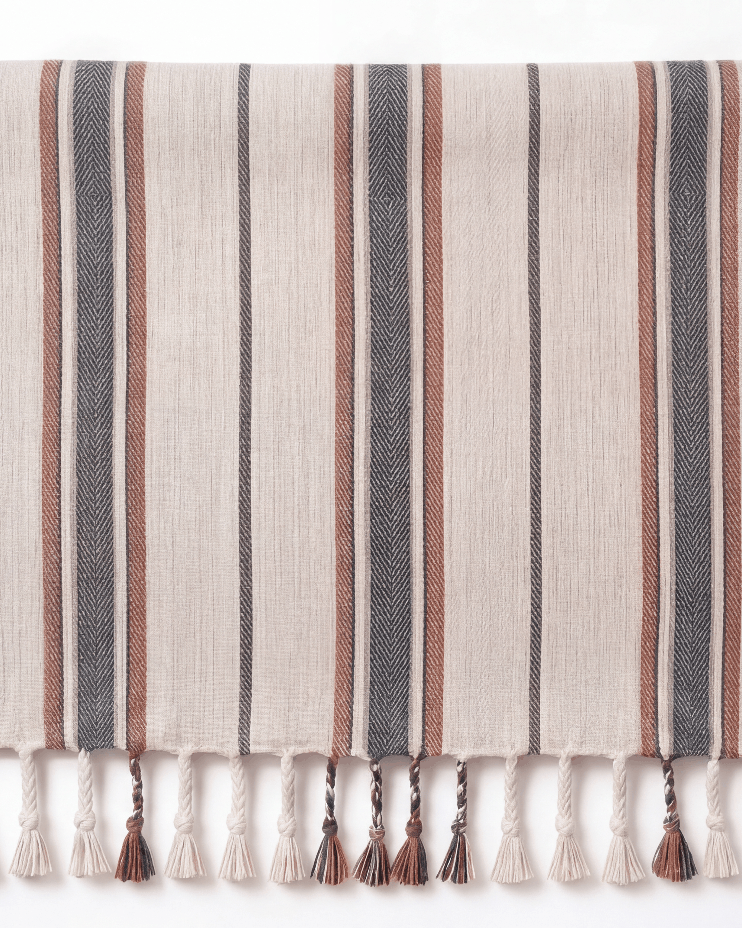 A rectangular woven towel with vertical stripes in beige, gray, and rust brown, finished with fringe tassels along the bottom edge. A small fabric label is stitched on the left side.