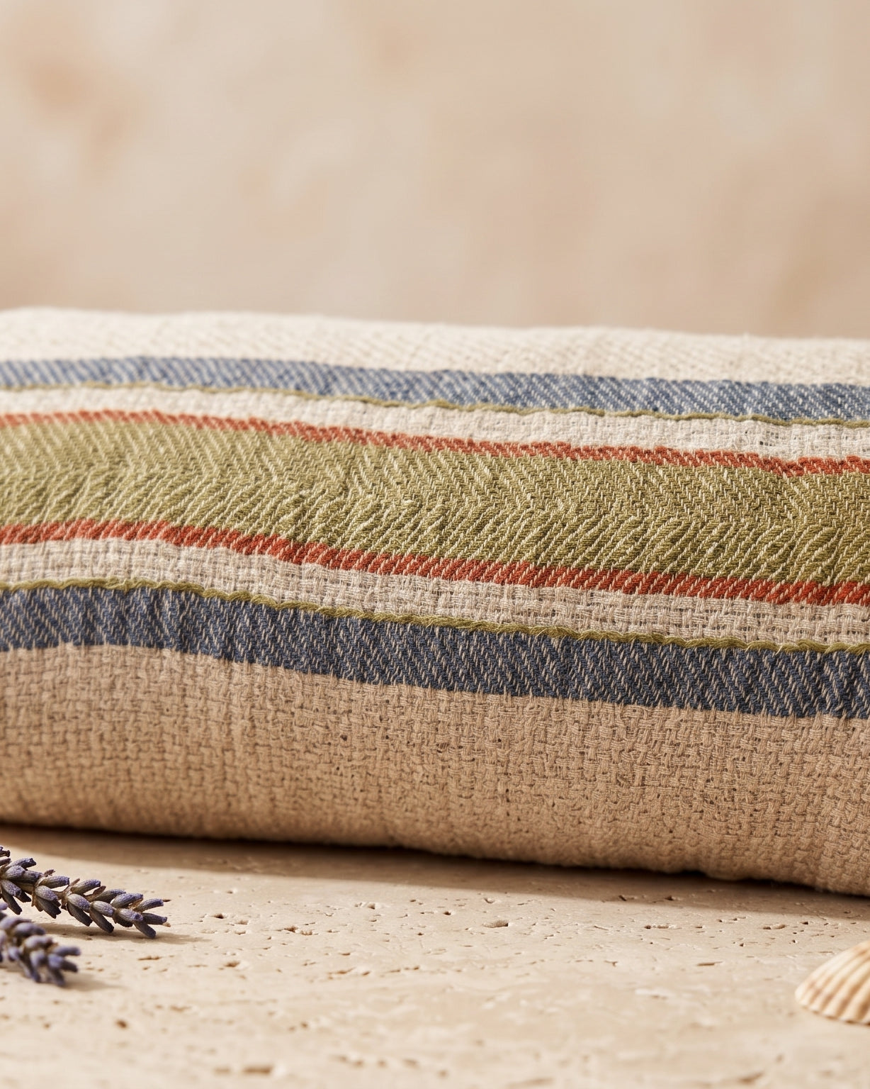 A striped cotton Turkish towel with fringed tassels, styled on a stone surface with a bar of soap, lavender sprigs, and seashells against a neutral beige background.
