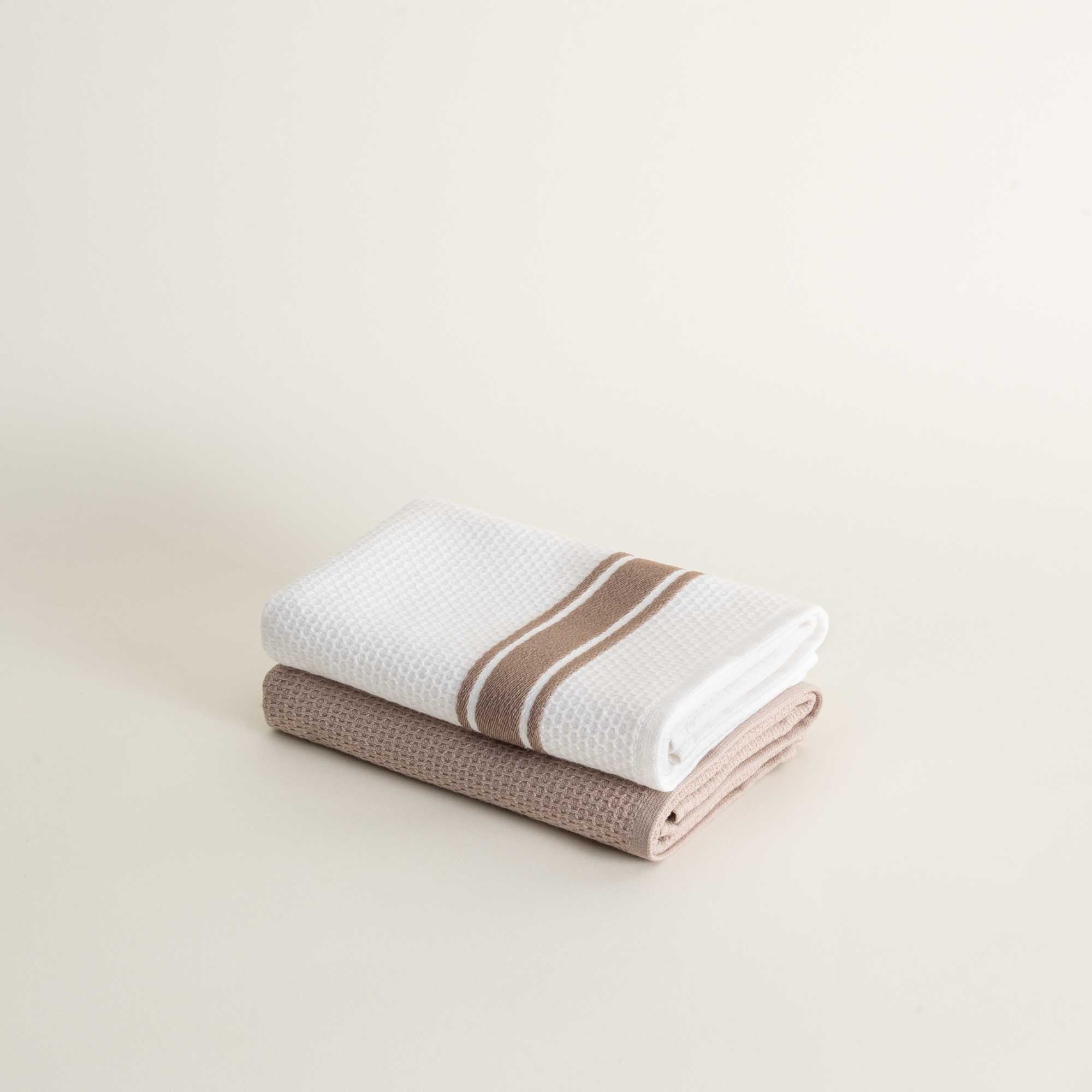 Two folded towels, one white with a brown stripe and one brown, on a light beige background.