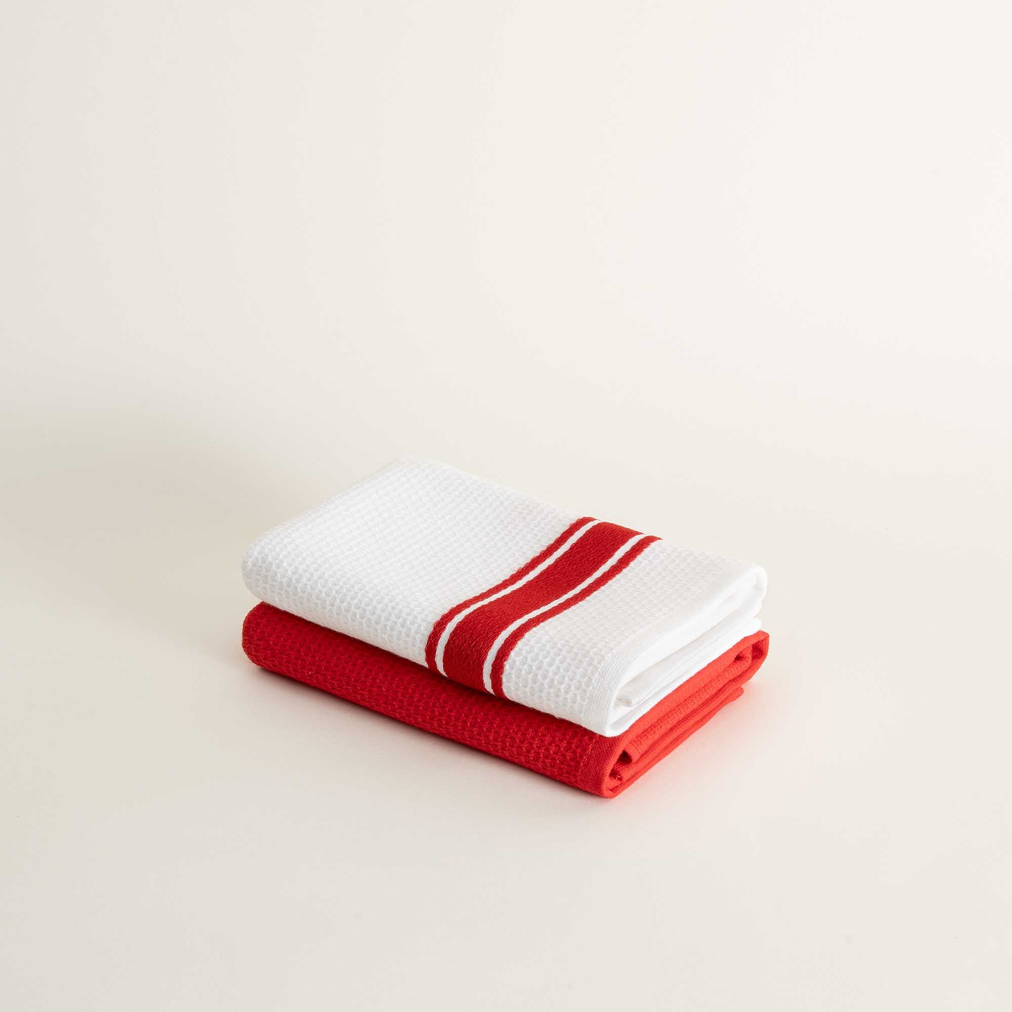 Two folded towels, one red and one white with a red stripe, on a light beige background.