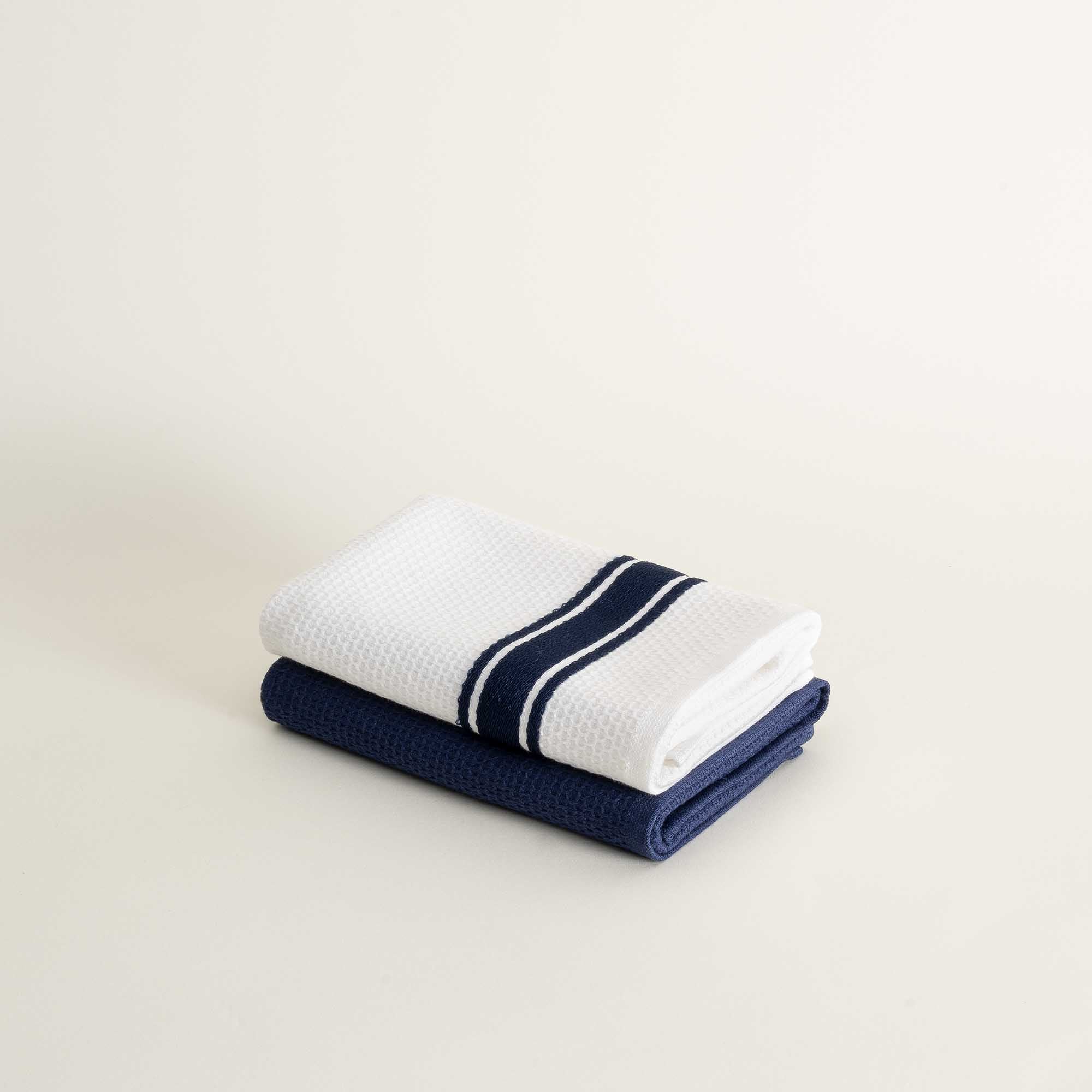Two folded towels, one white with blue stripes and one blue, on a light beige background.