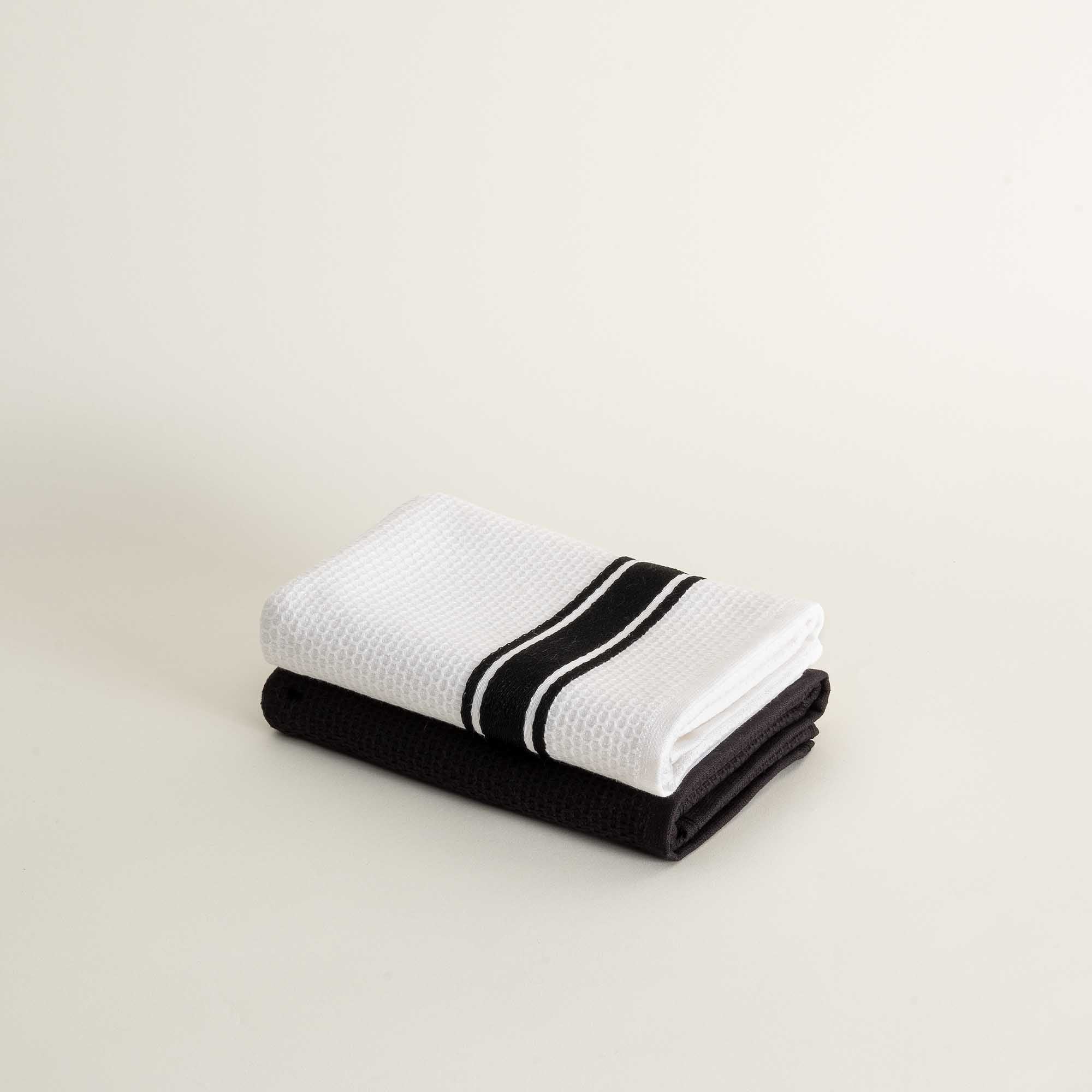 Two folded towels, one black and one white with a black stripe, on a light beige background.