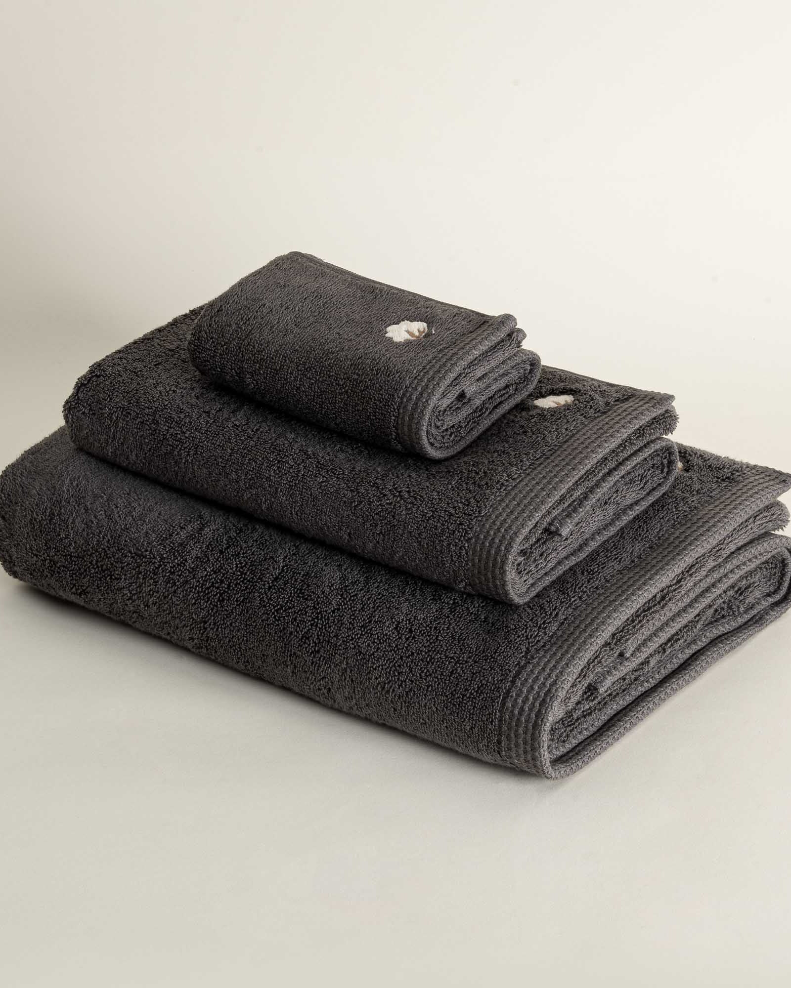 Side view of three folded Jasper 600-gram organic Aegean cotton luxury bath, hand, and washcloth towels in Charcoal Charm, highlighting soft plush texture, deep color, and luxurious fabric