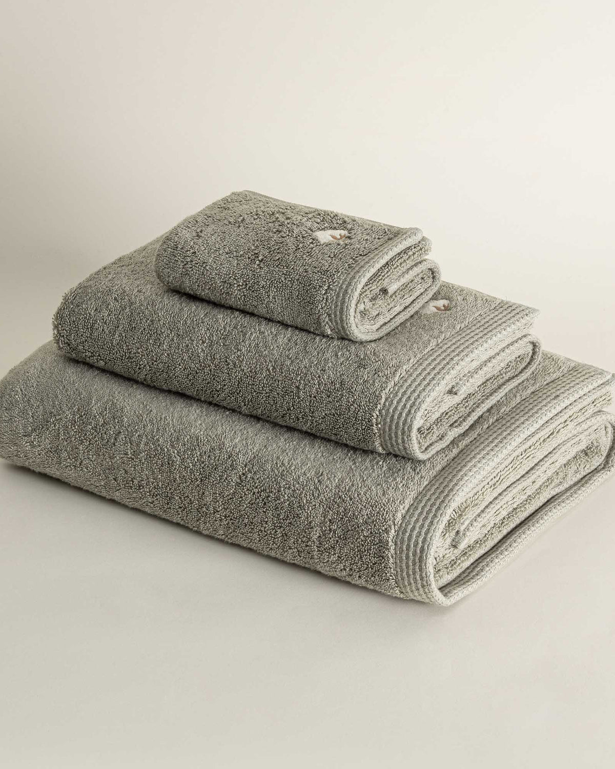 Side view of three folded Jasper 600-gram organic Aegean cotton luxury bath, hand, and washcloth towels in Mossy Muse, highlighting soft plush texture, earthy tone, and luxurious fabric