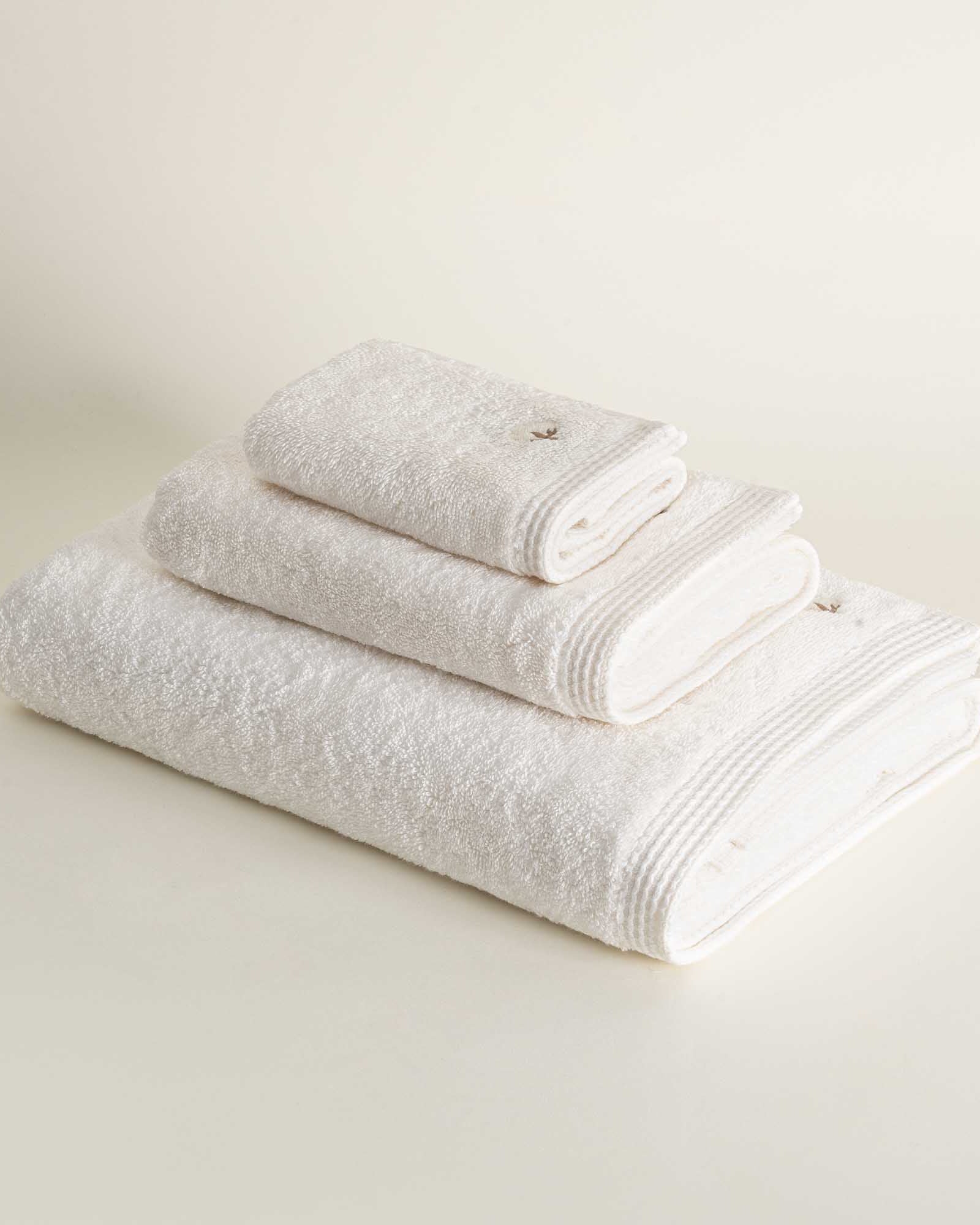 Side view of three folded Jasper 600-gram organic Aegean cotton luxury bath, hand, and washcloth towels in Ivory Embrace, highlighting soft plush texture, light tone, and luxurious fabric