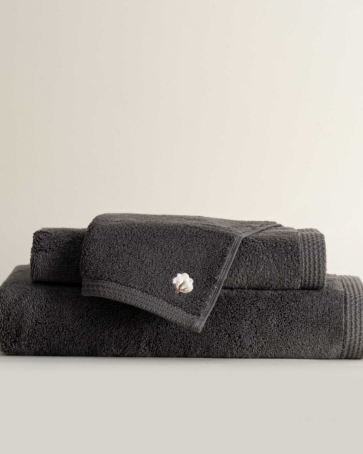 Three folded Jasper 600-gram organic Aegean cotton luxury bath, hand, and washcloth towels in Charcoal Charm, showcasing soft plush texture, deep color, and luxurious fabric