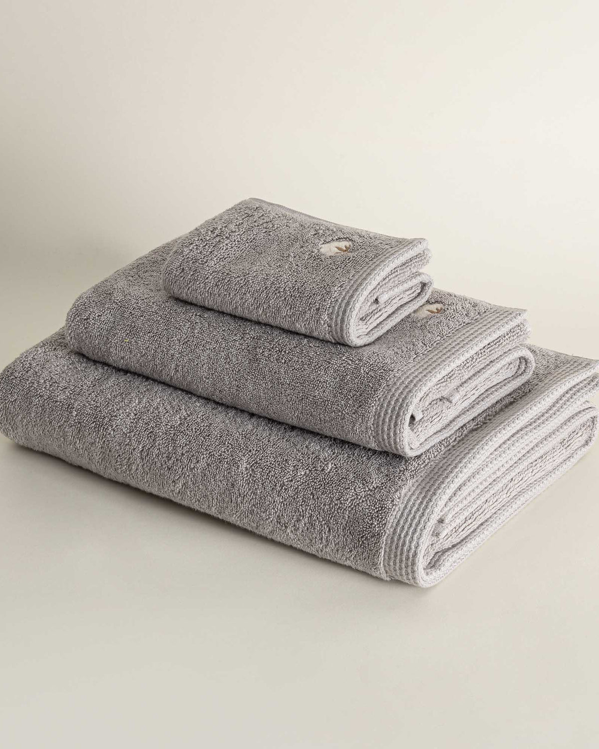 Side view of three folded Jasper 600-gram organic Aegean cotton luxury bath, hand, and washcloth towels in Silver Symphony, highlighting soft plush texture, cool tone, and luxurious fabric