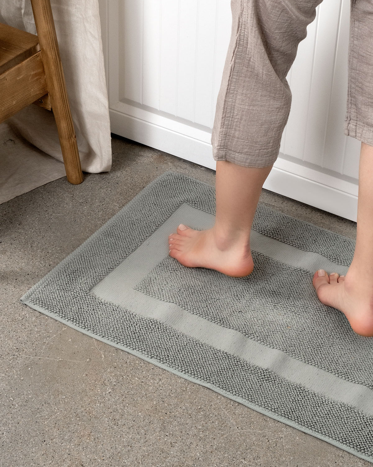 Kaia Aegean Cotton Bath Mat in Meadow Sage, gently stepped on, showcasing its soft texture, soothing colour, and luxurious fabric