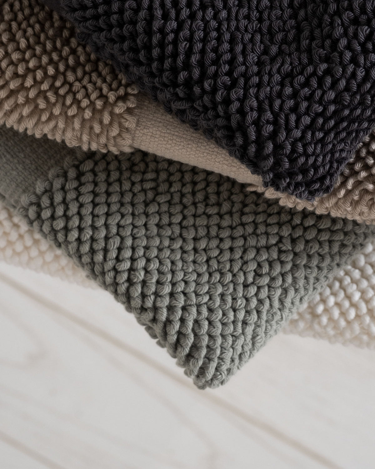 Kaia Aegean Cotton Bath Mats folded in four colours—Charcoal Charm, Whispering Sands, Meadow Sage, and Pearl Petal—showcasing their soft texture and harmonious palette