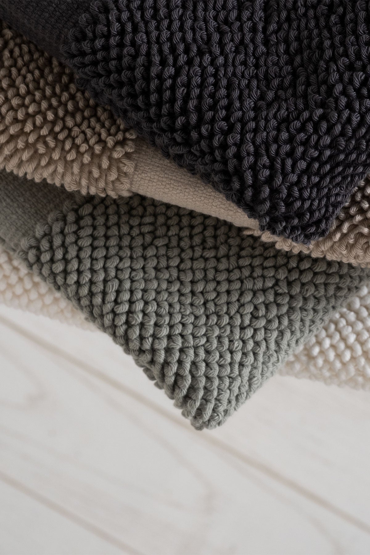 Kaia Aegean Cotton Bath Mats folded in four colours—Charcoal Charm, Whispering Sands, Meadow Sage, and Pearl Petal—showcasing their soft texture and harmonious palette