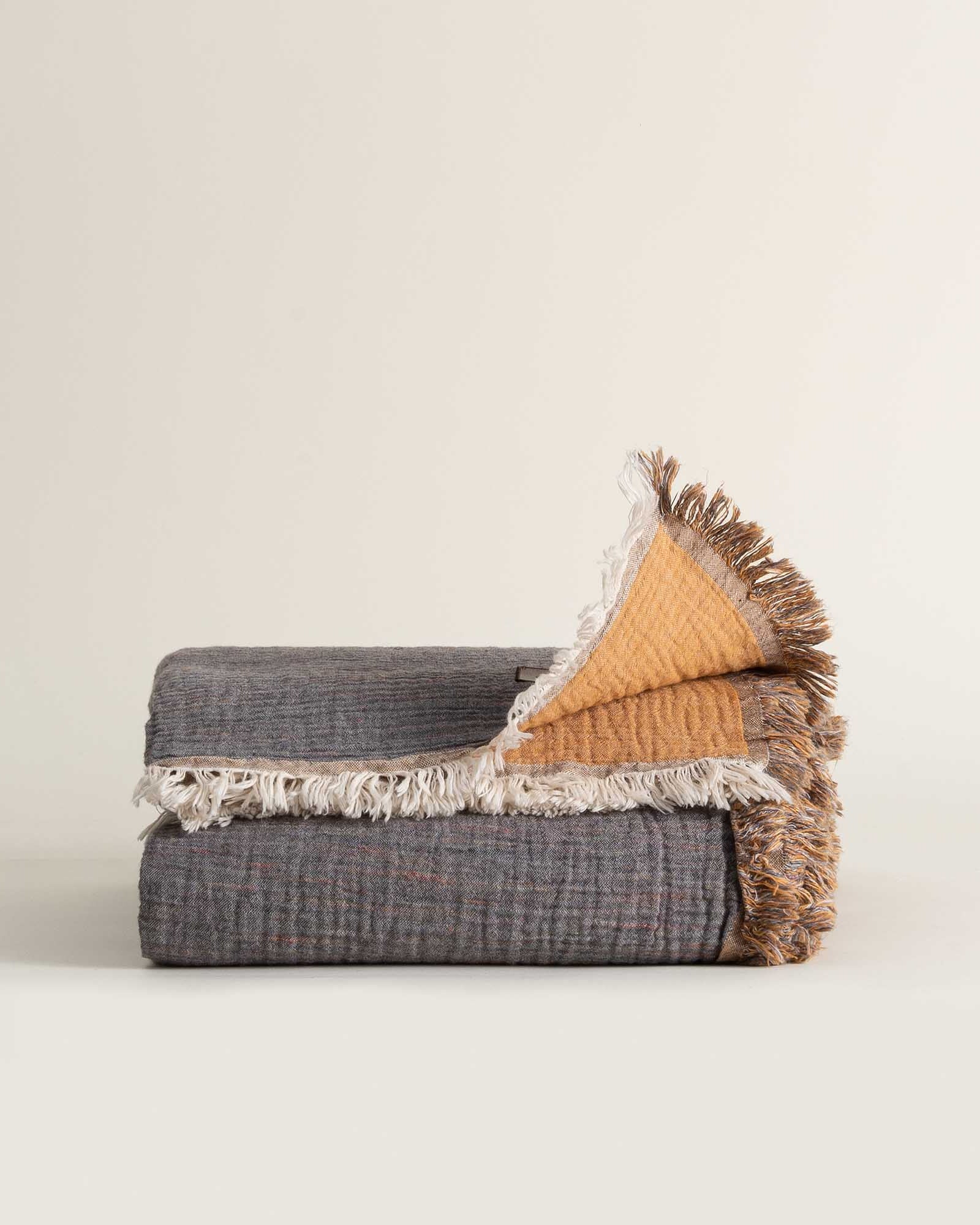 Folded reversible Muna organic gauze bed spread in Mustard, vibrant color, soft texture, neat folds with organic cotton sheets.