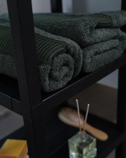 Green towels on a black shelf with a wooden brush and glass container in the background.