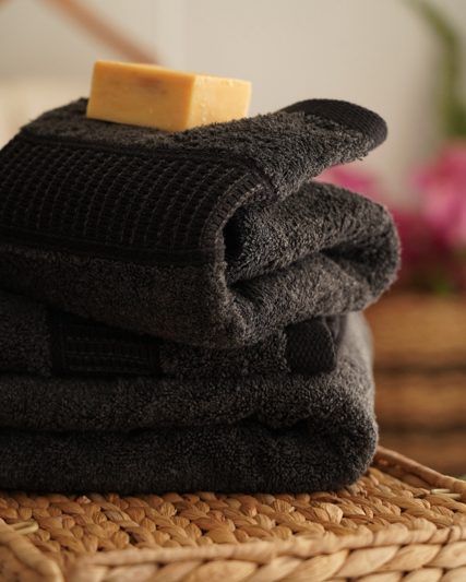 Stack of dark towels with a bar of soap on top, placed on a woven surface.