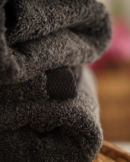 Stack of dark gray towels on a woven surface with a blurred background