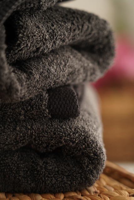 Stack of dark gray towels on a woven surface with a blurred background