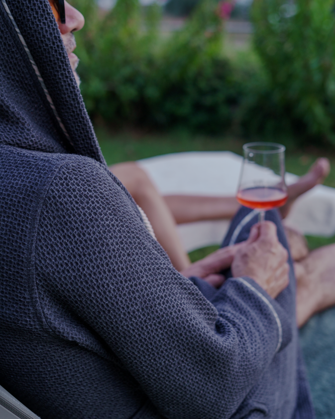 A male holding a glass of wine chilling with Minoa's luxuriously soft, organic Naia Panama Weave Mens Robe that provides extra comfort