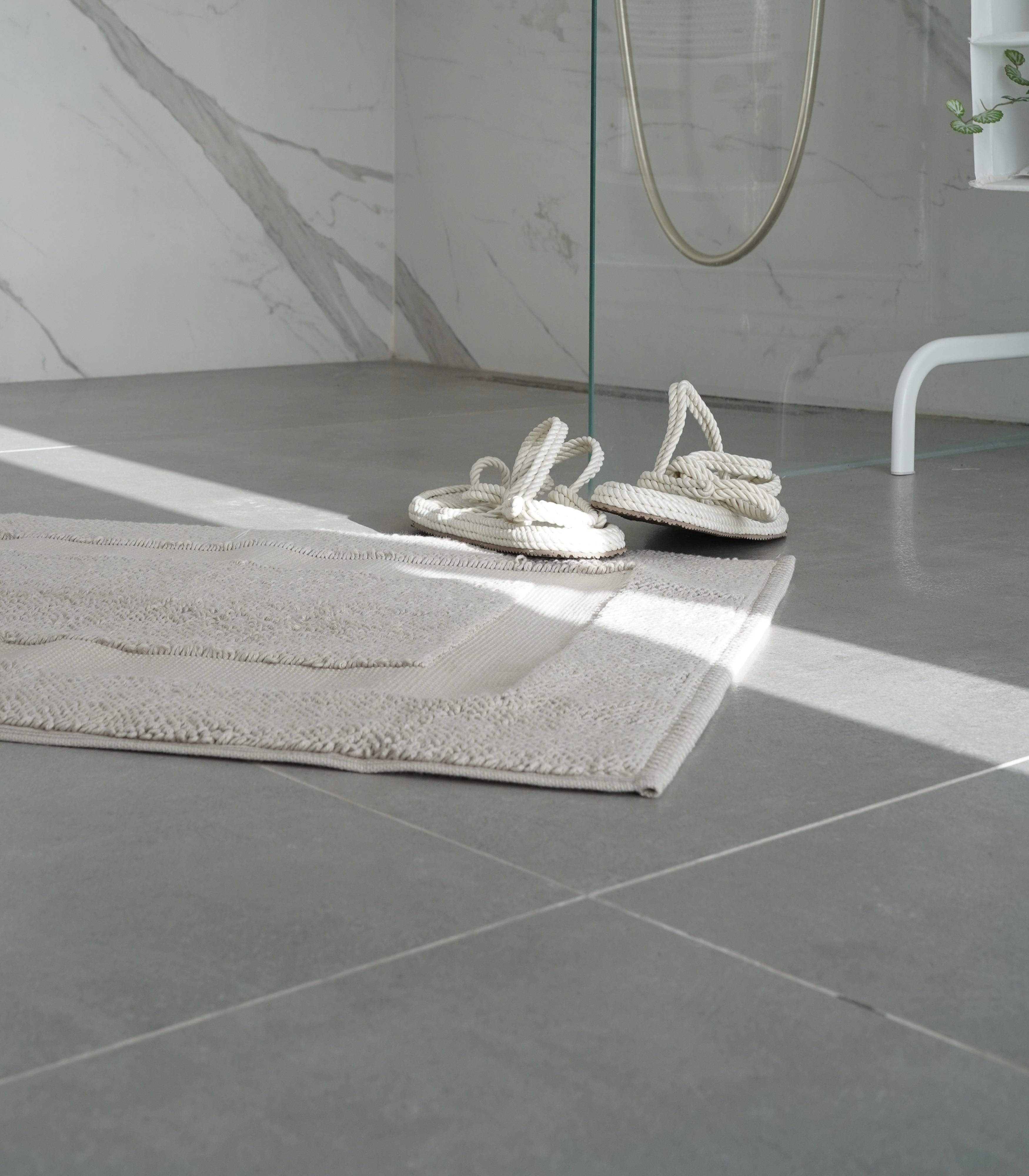 Kaia Aegean Cotton Bath Mat in Pearl Petal colour, placed in a shower room setting, showcasing its soft texture, elegant colour, and luxurious fabric