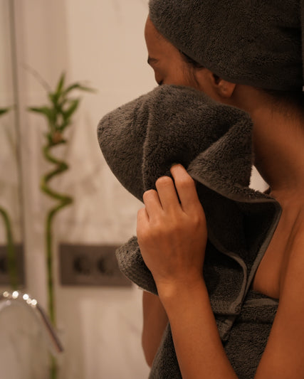 Woman wiping her face with Minoa USA Canada sustainable luxury bath towel from the Naia and cotton collection after a shower, showcasing soft, absorbent, and eco-friendly fabric