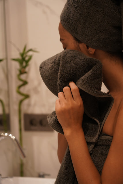 Woman wiping her face with Minoa USA Canada sustainable luxury bath towel from the Naia and cotton collection after a shower, showcasing soft, absorbent, and eco-friendly fabric