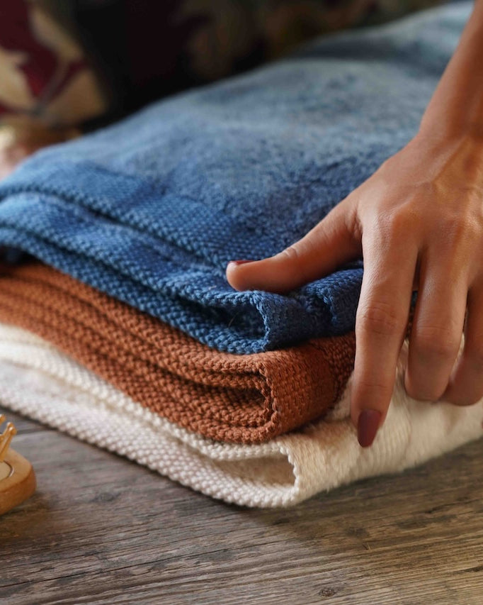 Person folding towels on a wooden surface with a wooden brush nearby