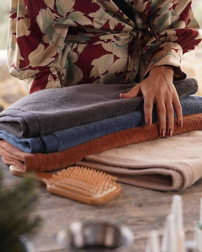 Person folding towels on a wooden surface with a blurred natural background