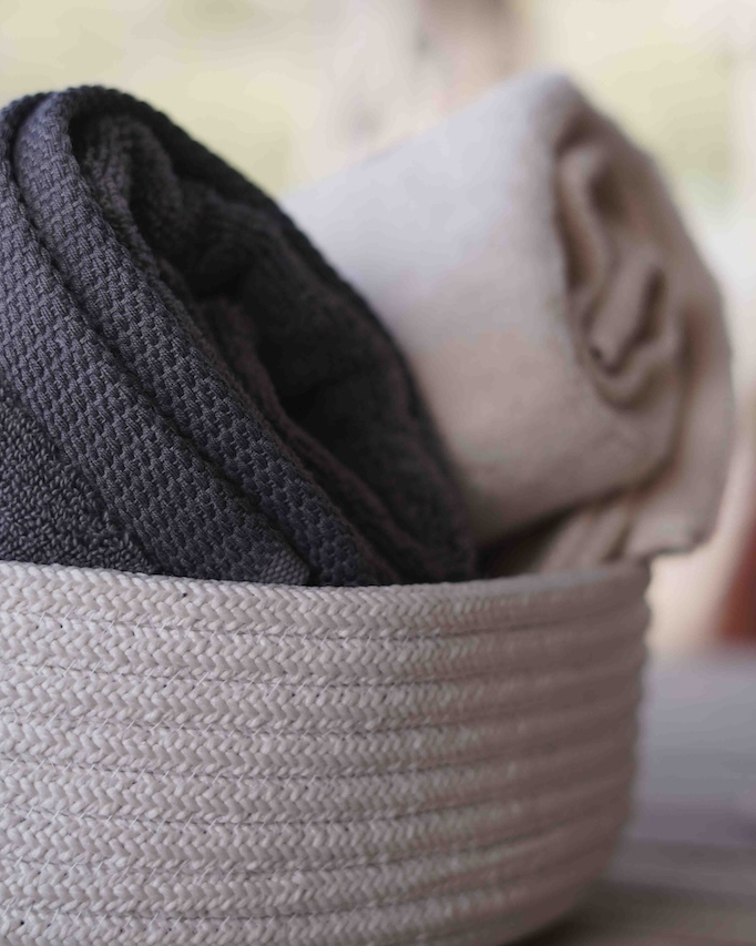Folded dark gray and beige towels in a woven basket with a blurred background
