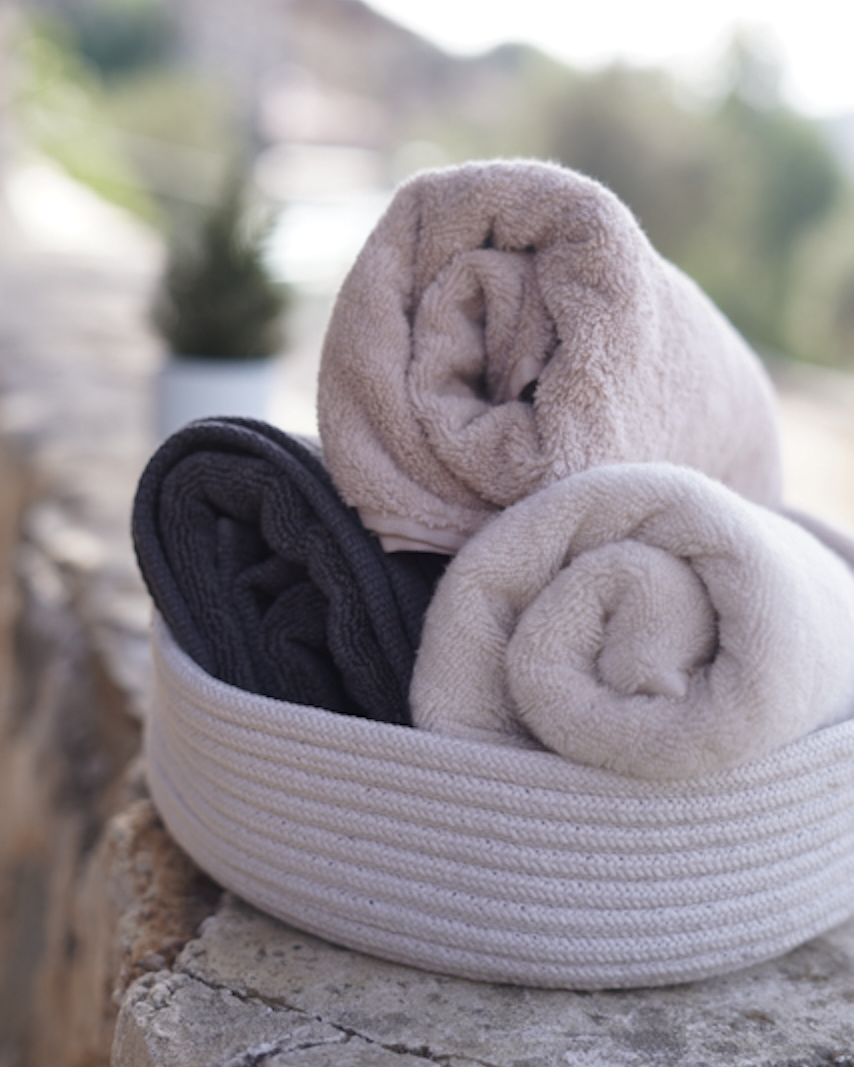 Three folded towels in a woven basket on stone steps with a blurred natural background