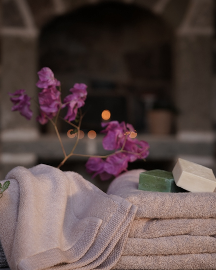 Folded towels with a bar of soap and purple flowers on a wooden surface with a blurred background.