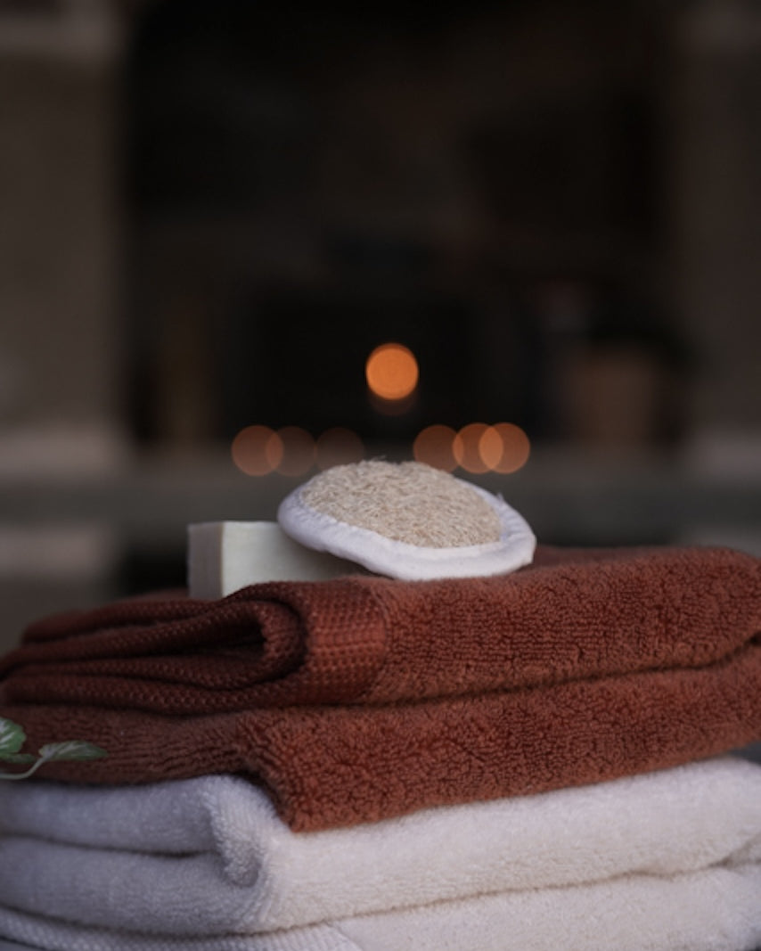 Stack of folded towels with a soap bar and loofah on a wooden surface, blurred background