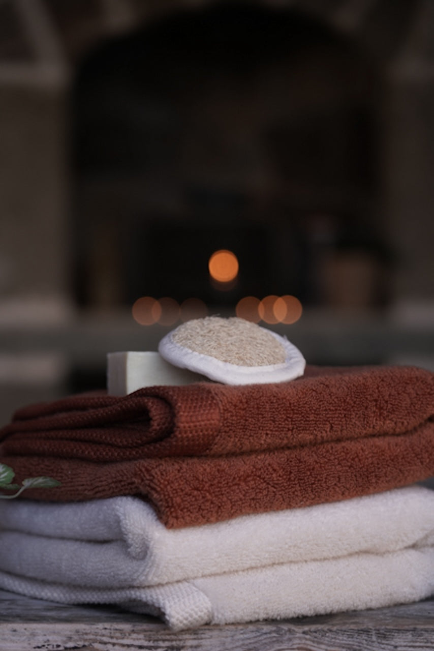 Stack of folded towels with a soap bar and loofah on a wooden surface, blurred background
