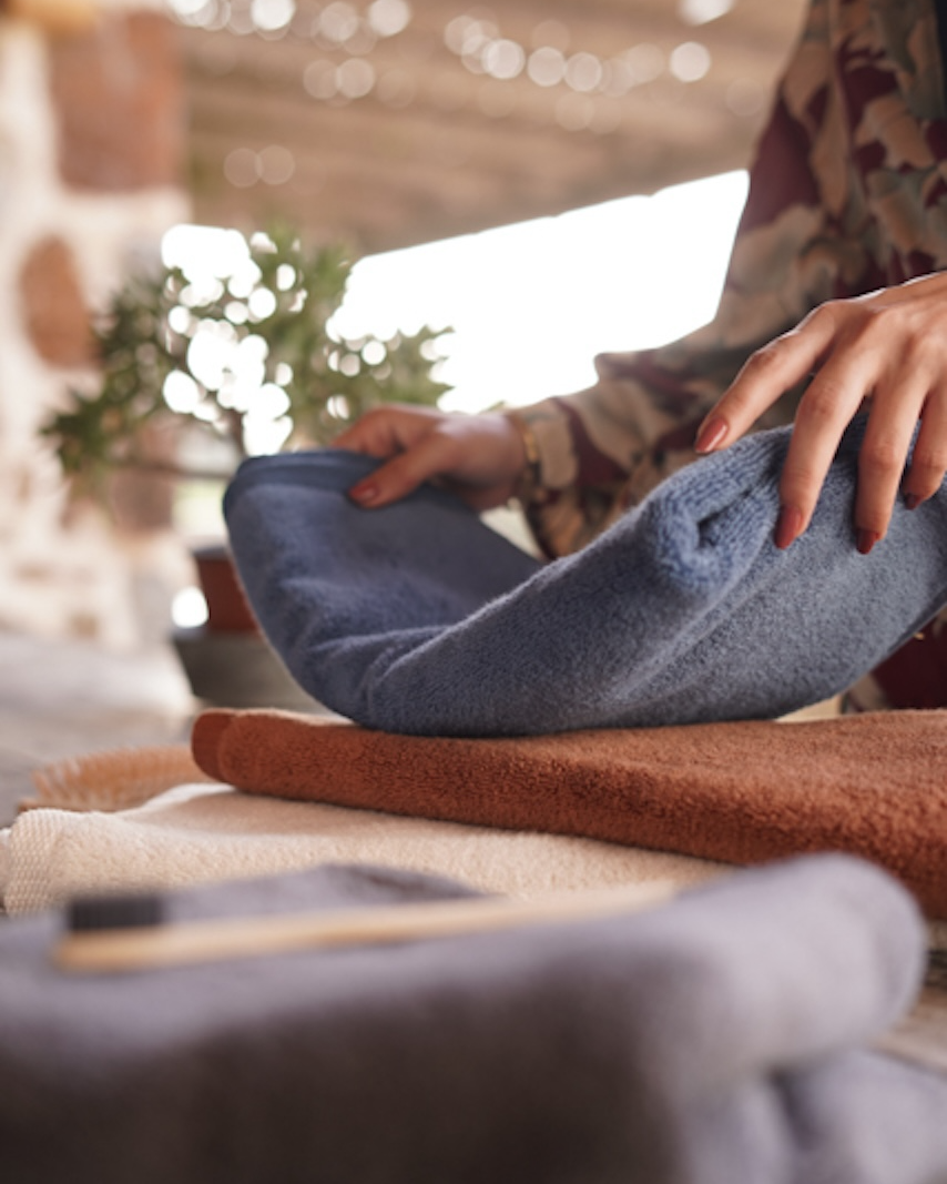 A person laying a blue towel on top of an orange towel on a table.