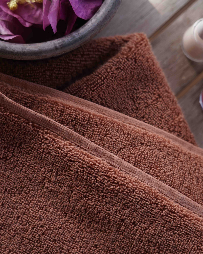 Brown towel on a wooden surface with bottles and a bowl in the background
