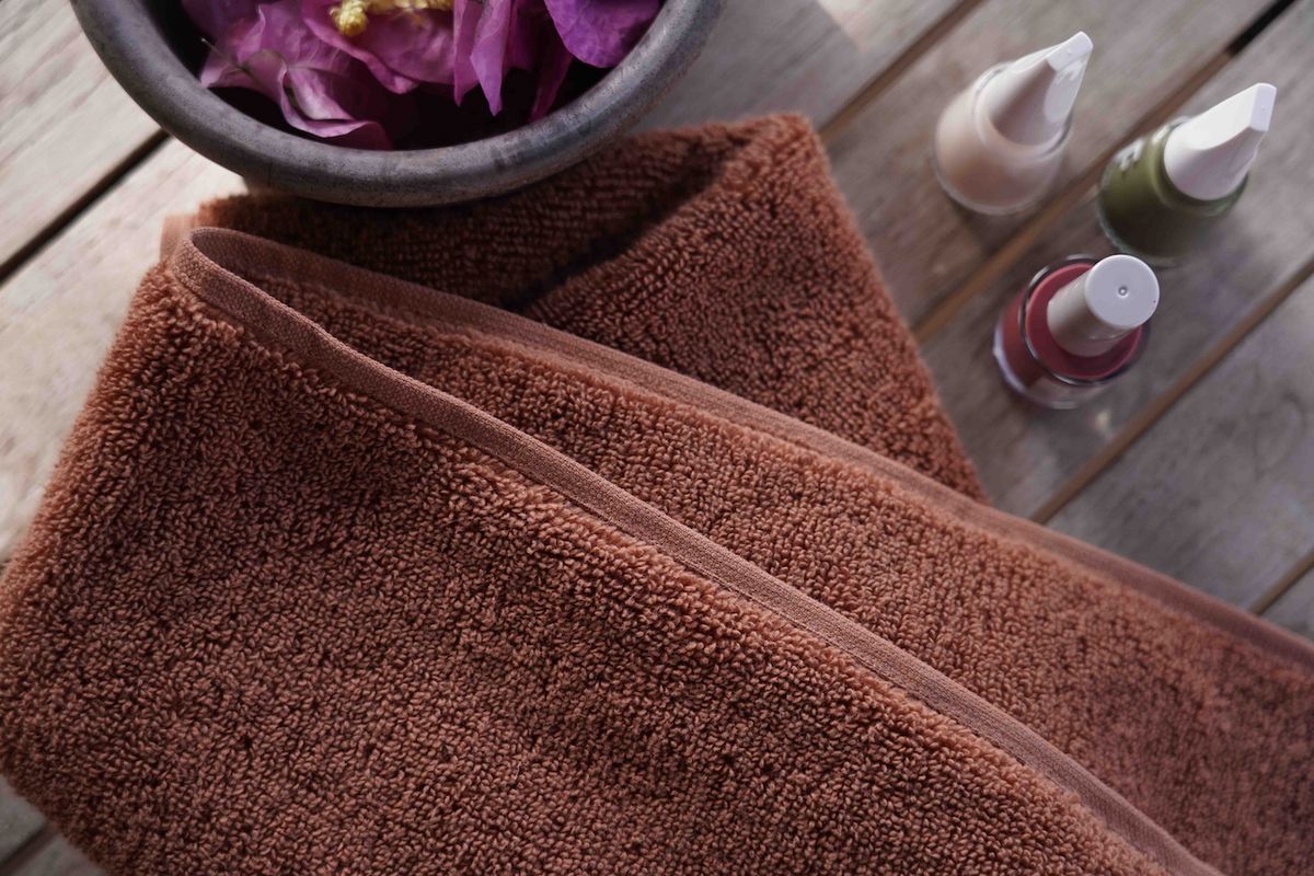 Brown towel on a wooden surface with bottles and a bowl in the background