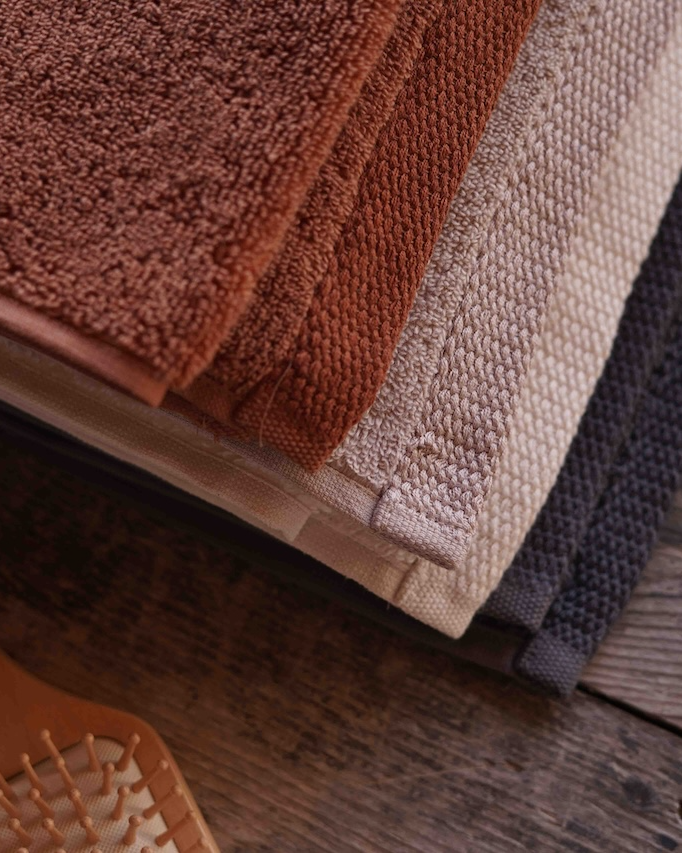 Stack of brown, beige, and gray towels on a wooden surface with a hairbrush.