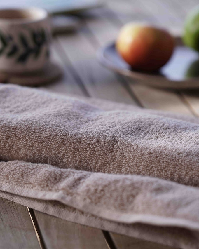 Brown towel on a wooden surface with a blurred background of a cup and fruits.
